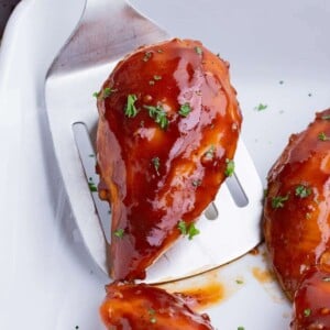 A spatula scoops a baked chicken breast out of the pan.