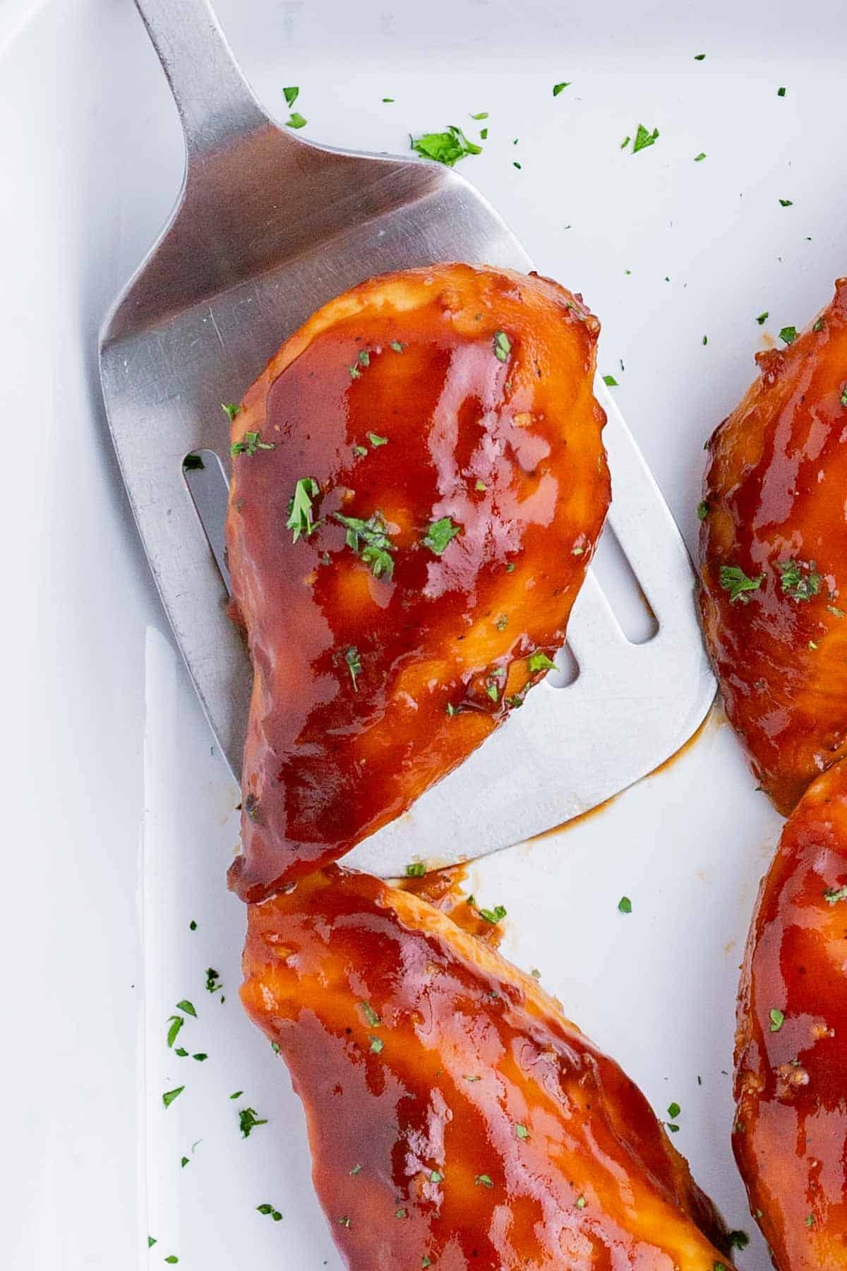 A spatula scoops a baked chicken breast out of the pan.