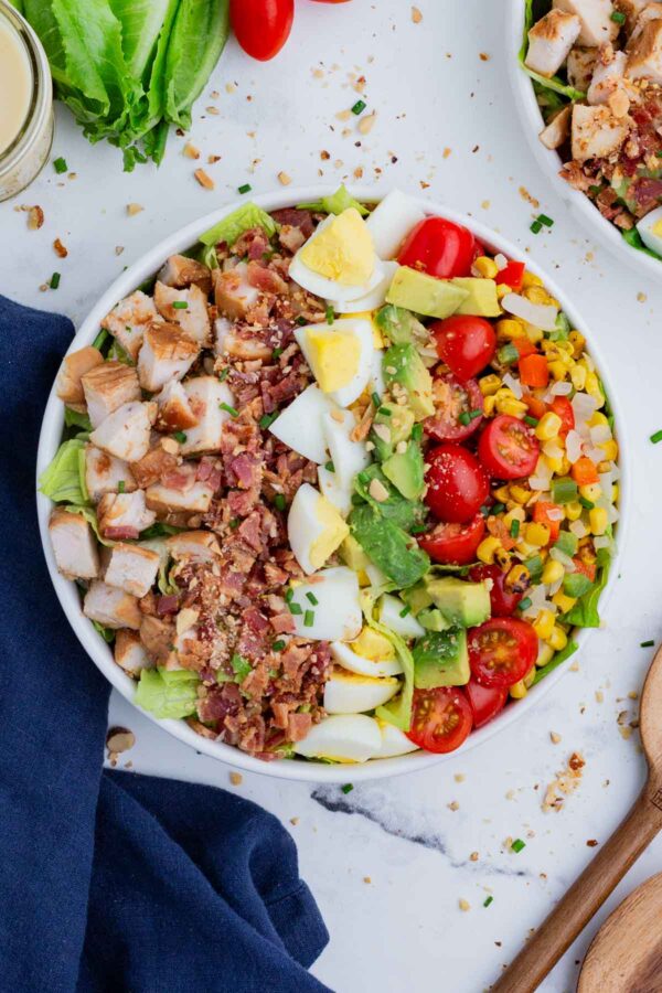 An overhead shot of a Cobb salad in a white bowl, with all the essential ingredients plus BBQ chicken.