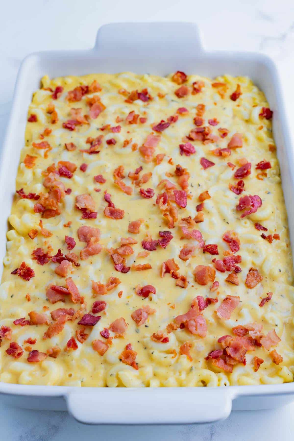 Cheesy noodles are added to a baking dish and topped with bacon.