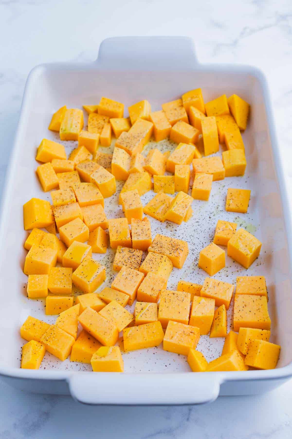 Cubed butternut squash in a white casserole dish ready for the oven.