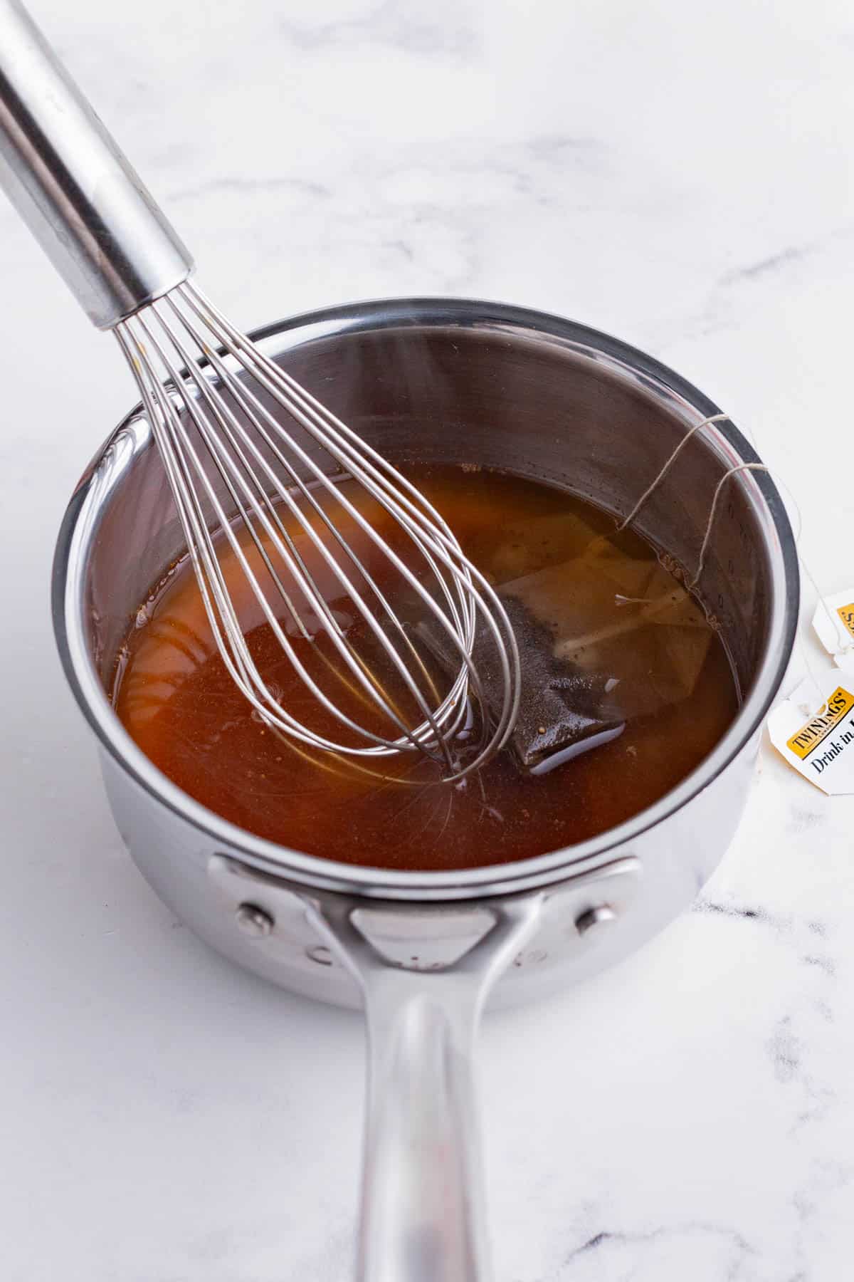 Black tea bags are added to water with sweetener and spices and heated on the stove.