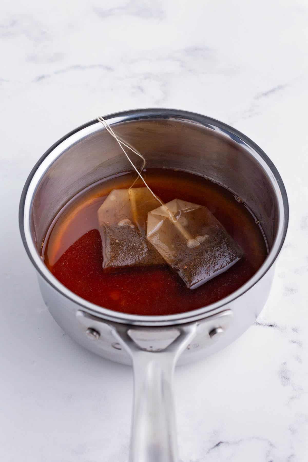 Black tea bags are added to water with sweetener and spices and heated on the stove.