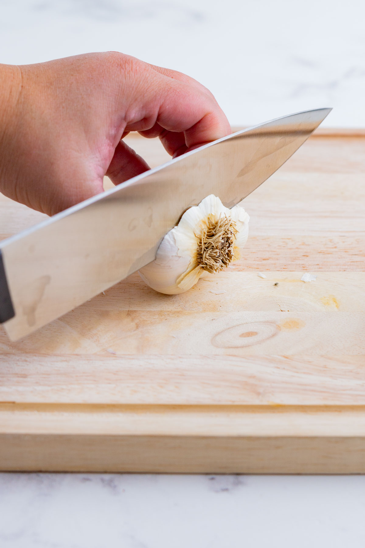 A knife cutting into a whole, unpeeled garlic head/bulb.