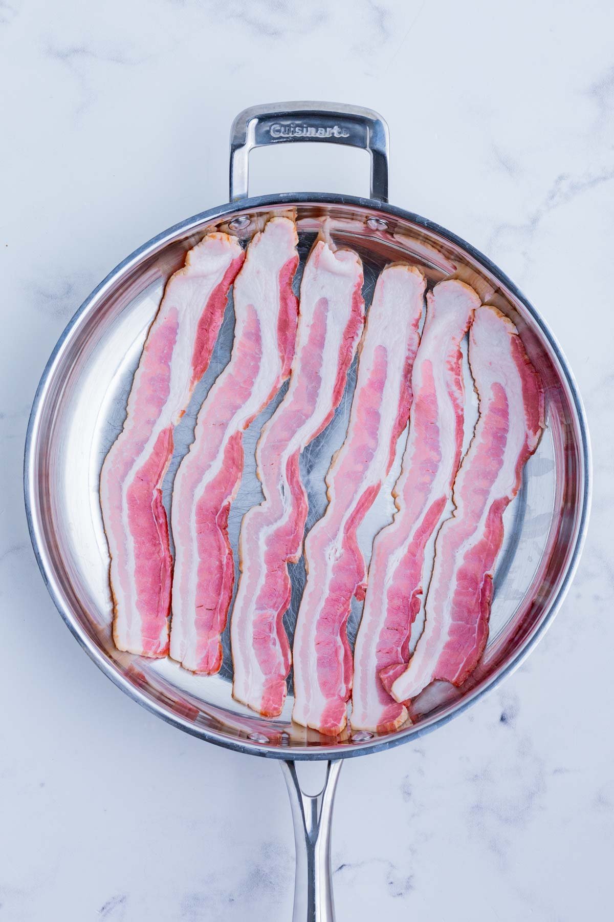 Raw bacon is lined up in a skillet.