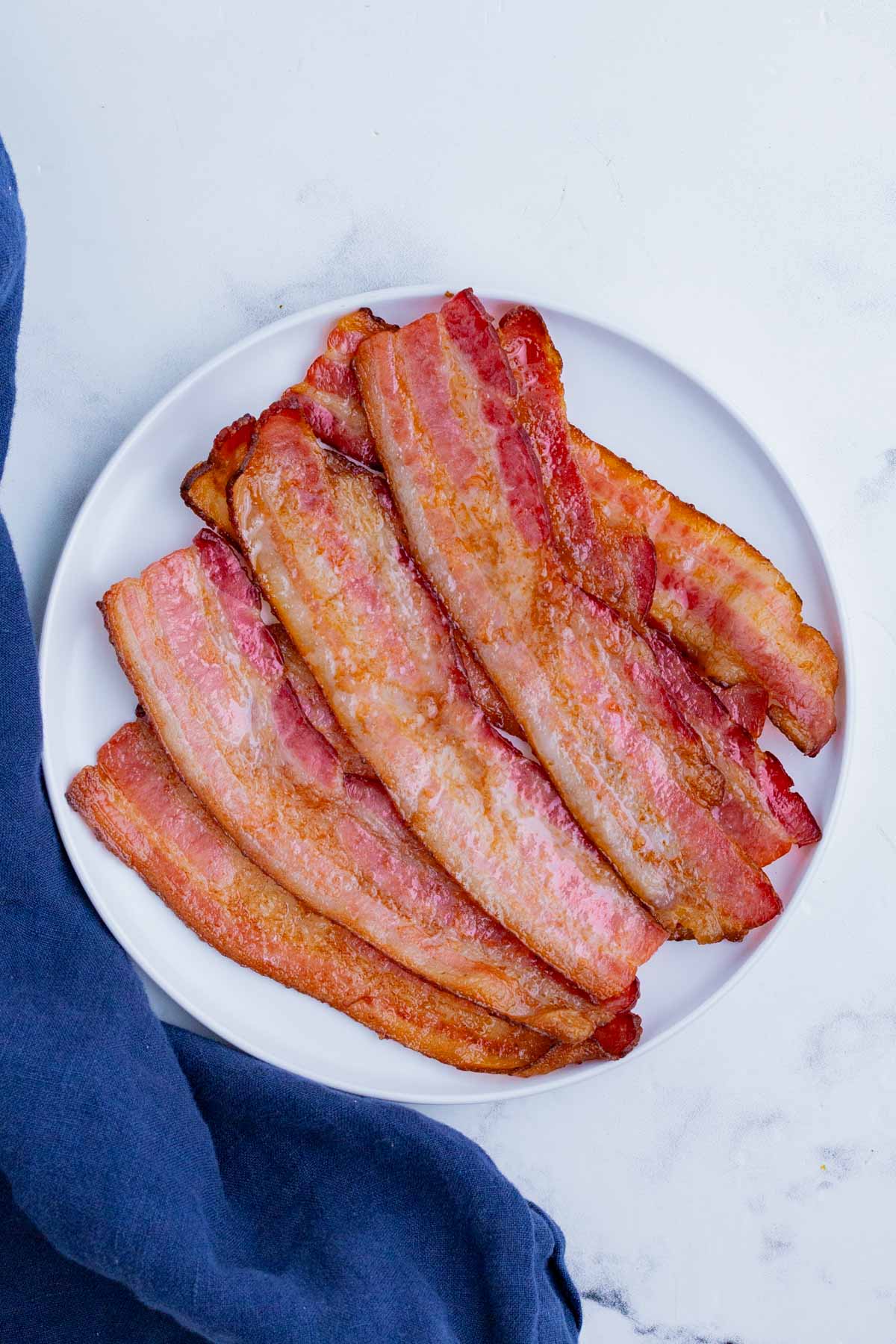 A white plate is loaded up with cooked bacon pieces.