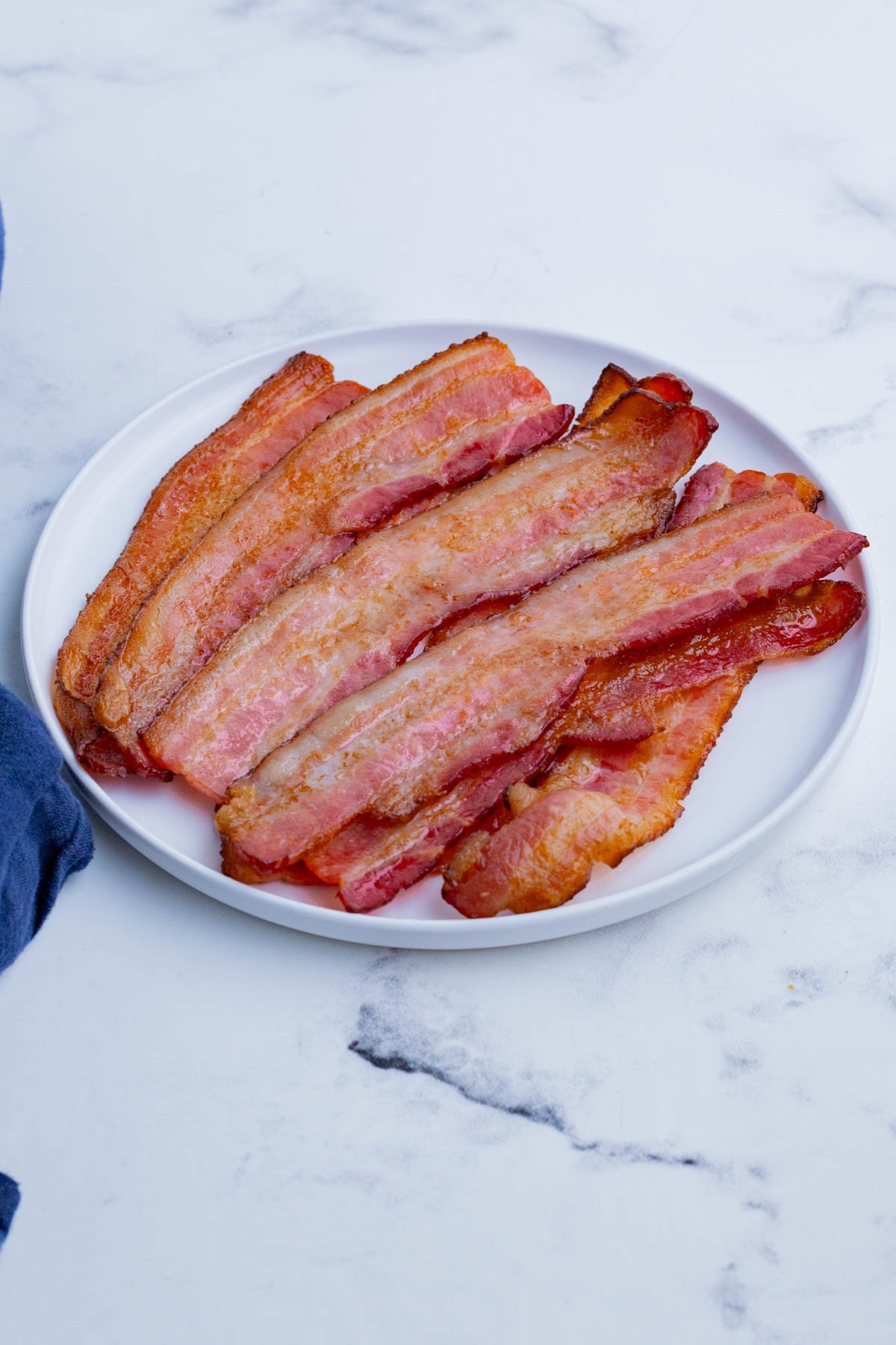 A white plate is loaded up with cooked bacon pieces.