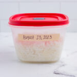 A small tupperware container with rice inside and labeled with a date.