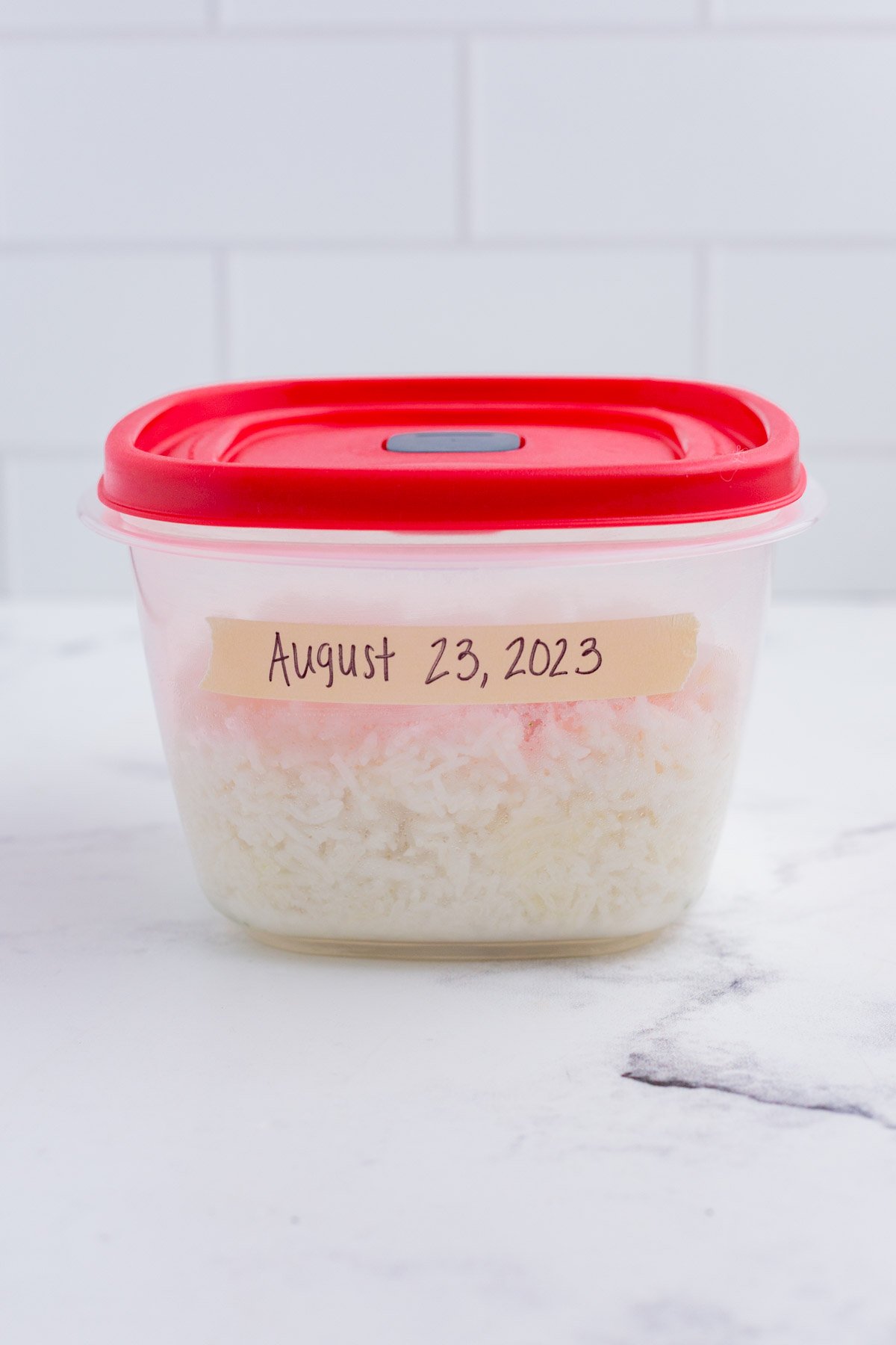 A small tupperware container with rice inside and labeled with a date.