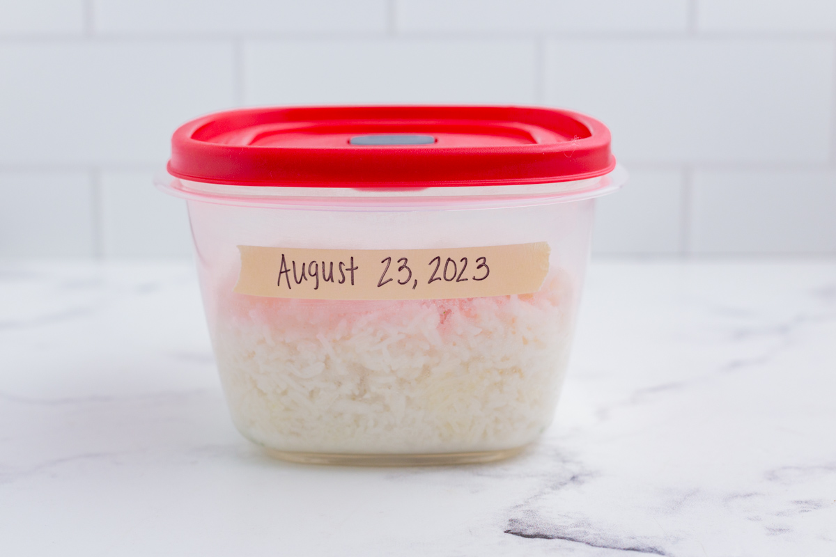 A small tupperware container with rice inside and labeled with a date.