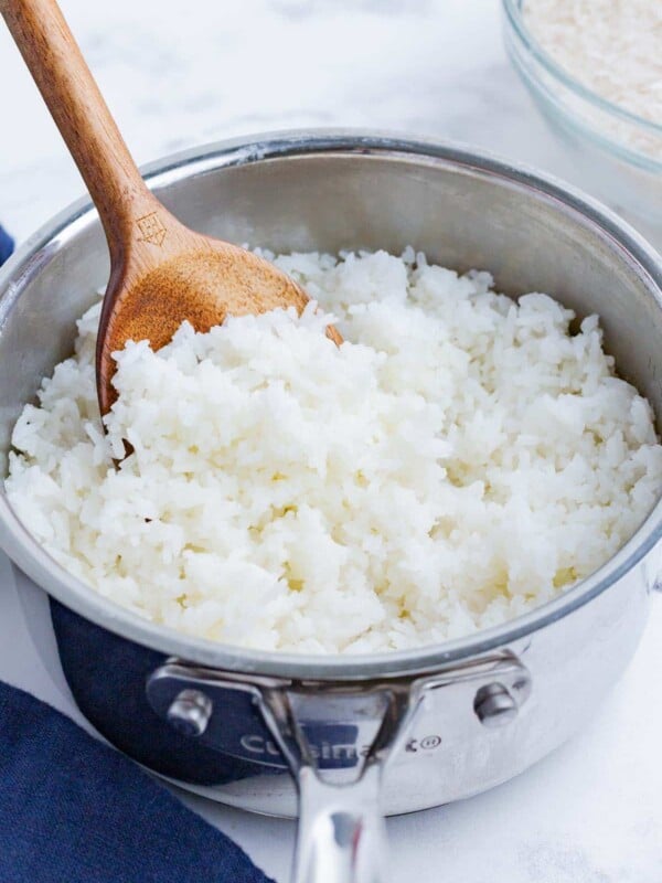 A wooden spoon stirs cooked white rice in a pot.