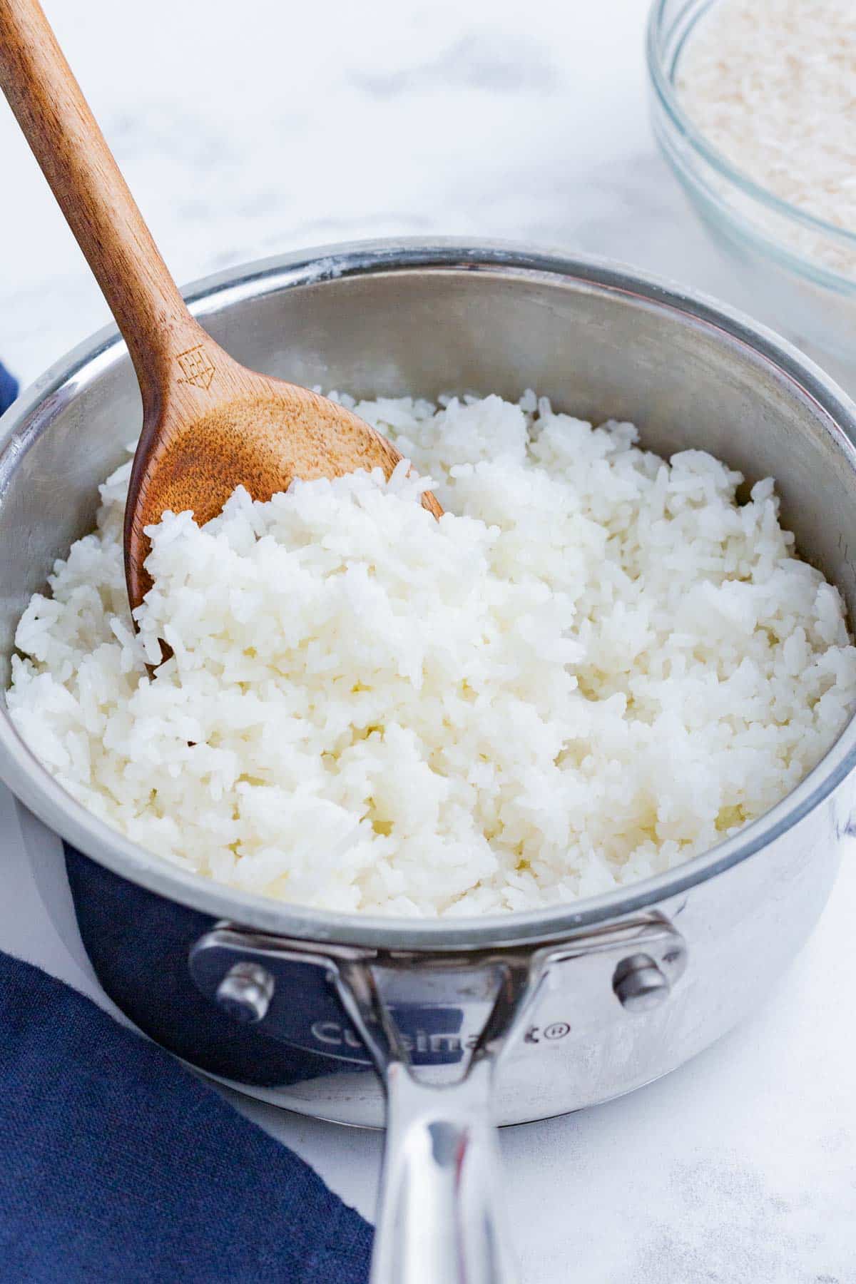 A wooden spoon stirs cooked white rice in a pot.