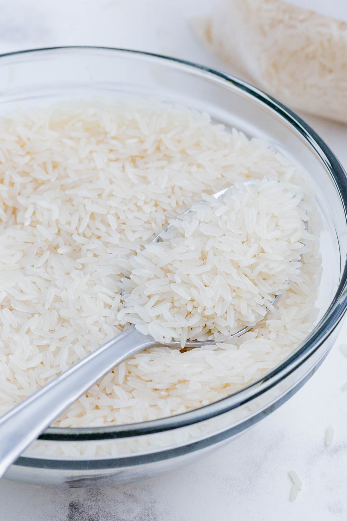 A spoon scoops Jasmine rice out of a glass bowl.