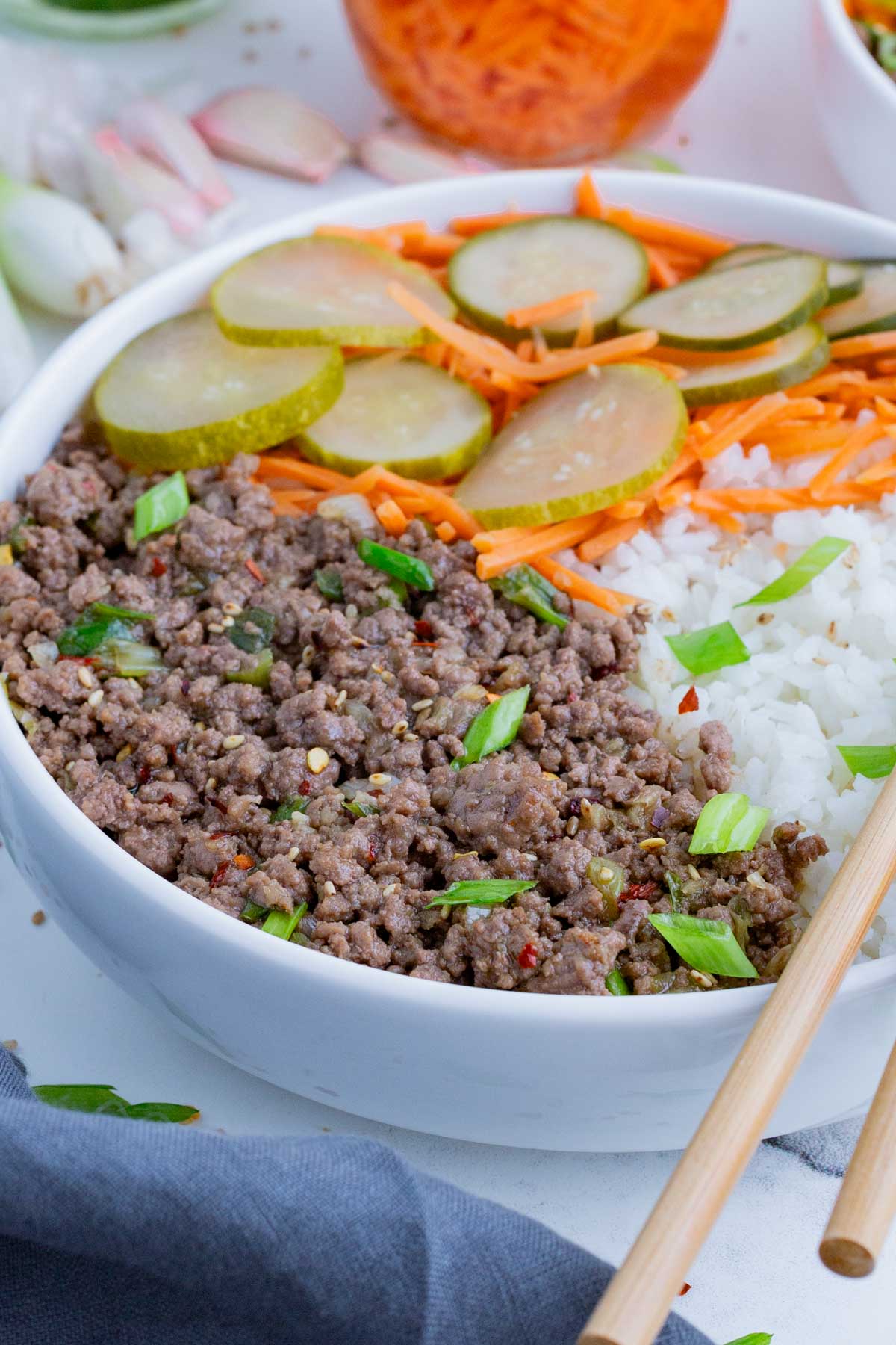 Korean beef is served in a white bowl with rice and pickled veggies.