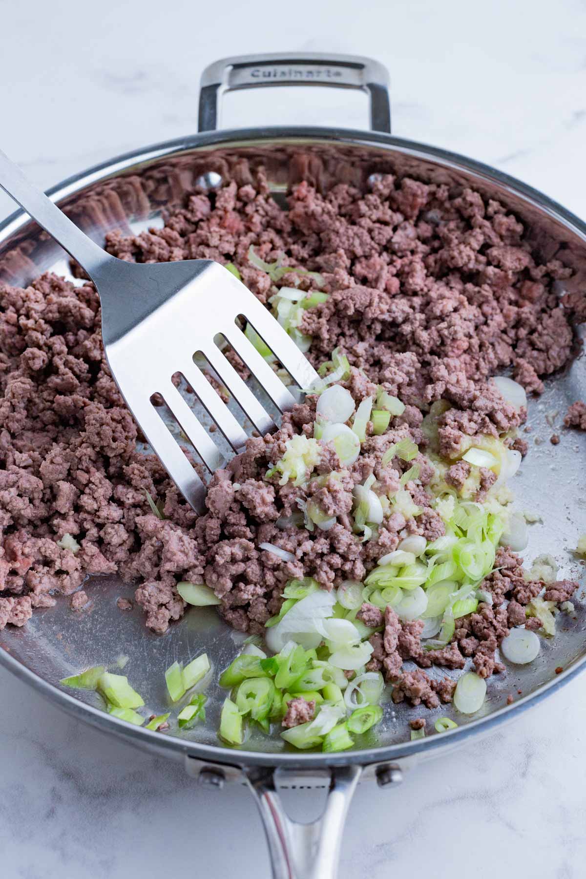 Veggies are added to the beef in the skillet.