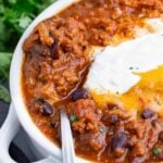 A white bowl of pumpkin chili is topped with traditional chili toppings.