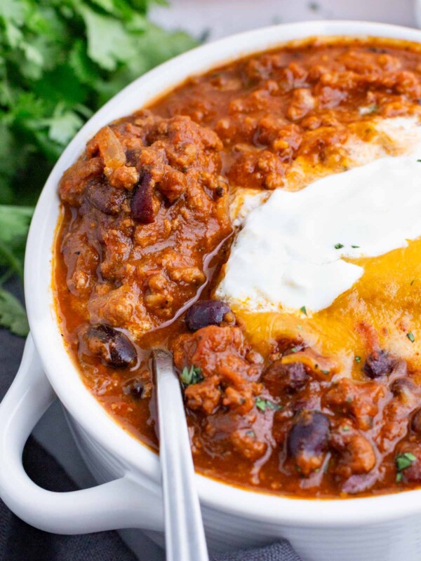 A white bowl of pumpkin chili is topped with traditional chili toppings.