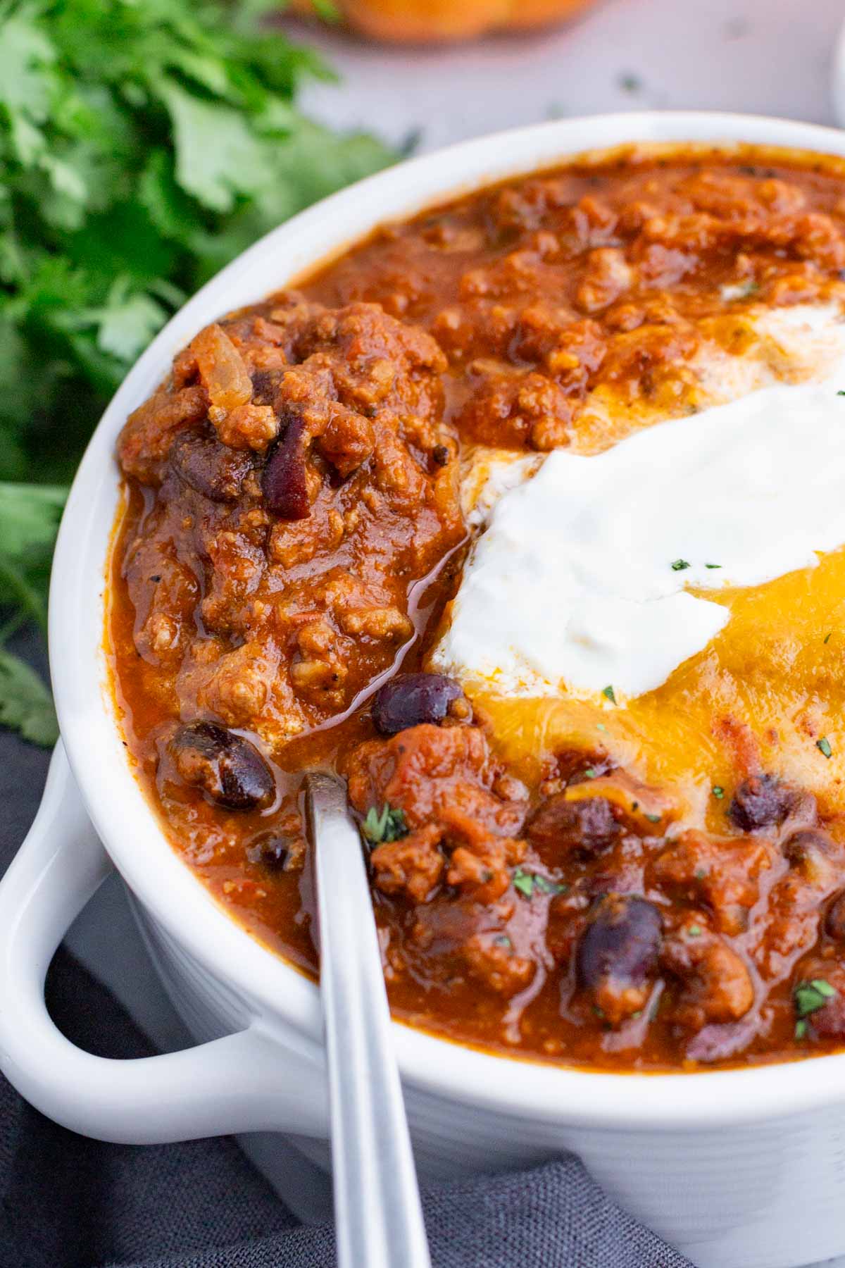 A white bowl of pumpkin chili is topped with traditional chili toppings.