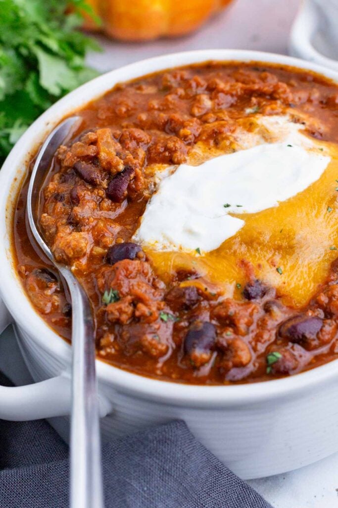 A white bowl of pumpkin chili is topped with traditional chili toppings.