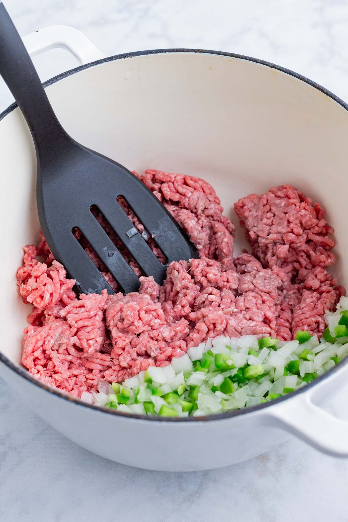 Ground beef is cooked in a pot by the veggies.