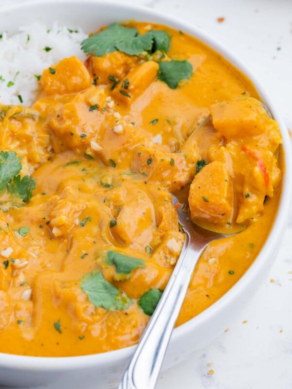 A spoon digs into a bowl full of pumpkin curry and white rice.