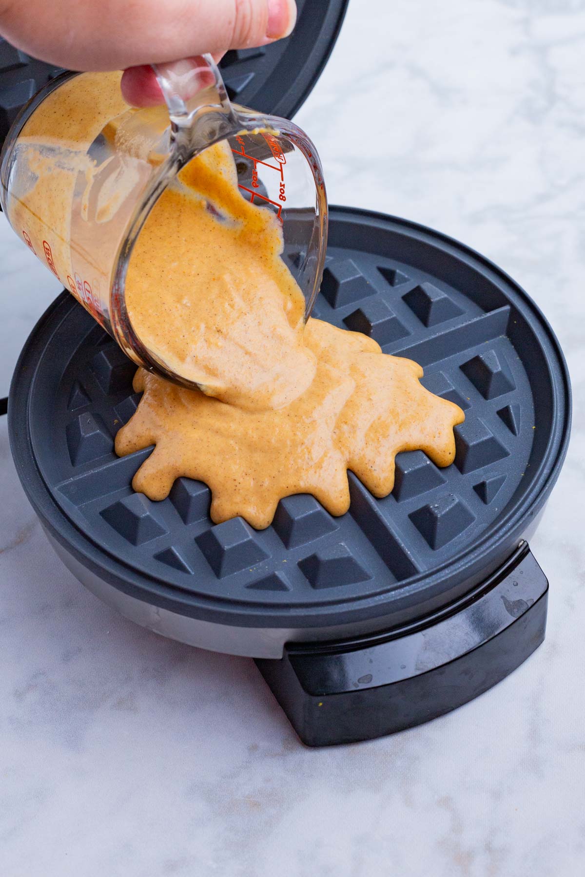 The pumpkin waffle batter is poured into a waffle iron.