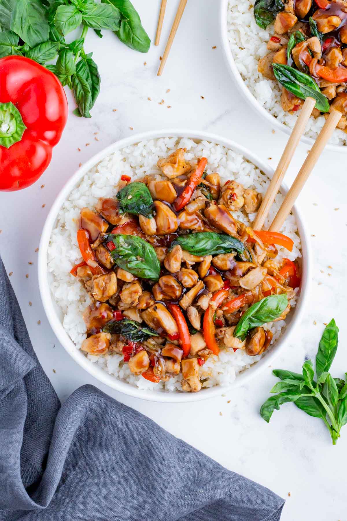 An overhead shot of Thai basil chicken stir fry in a white bowl with rice.
