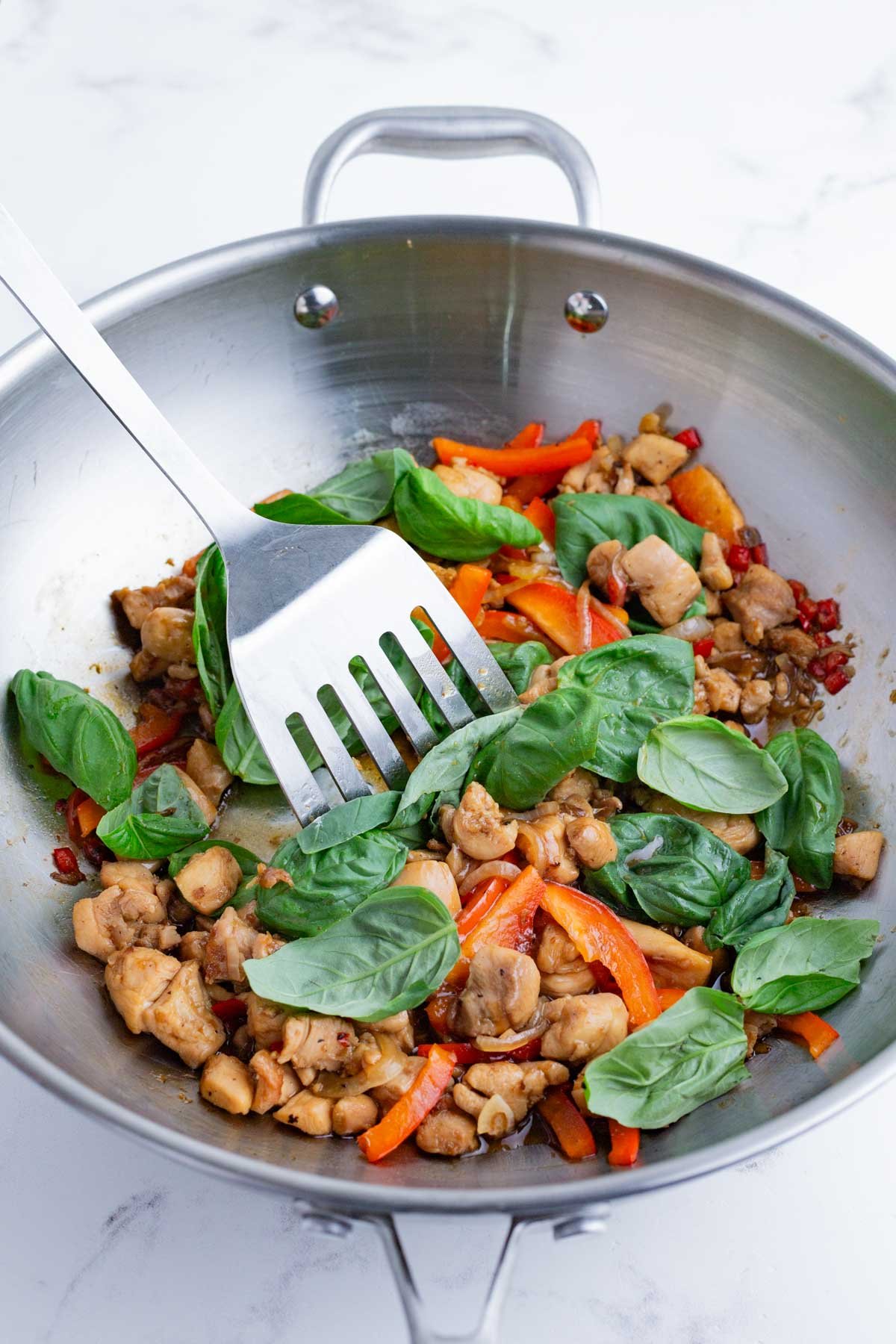 Basil is added to the wok with the chicken.