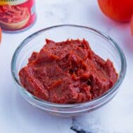 A bowl of tomato paste with a can and fresh tomato on the counter.