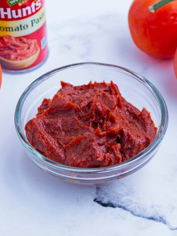 A bowl of tomato paste with a can and fresh tomato on the counter.