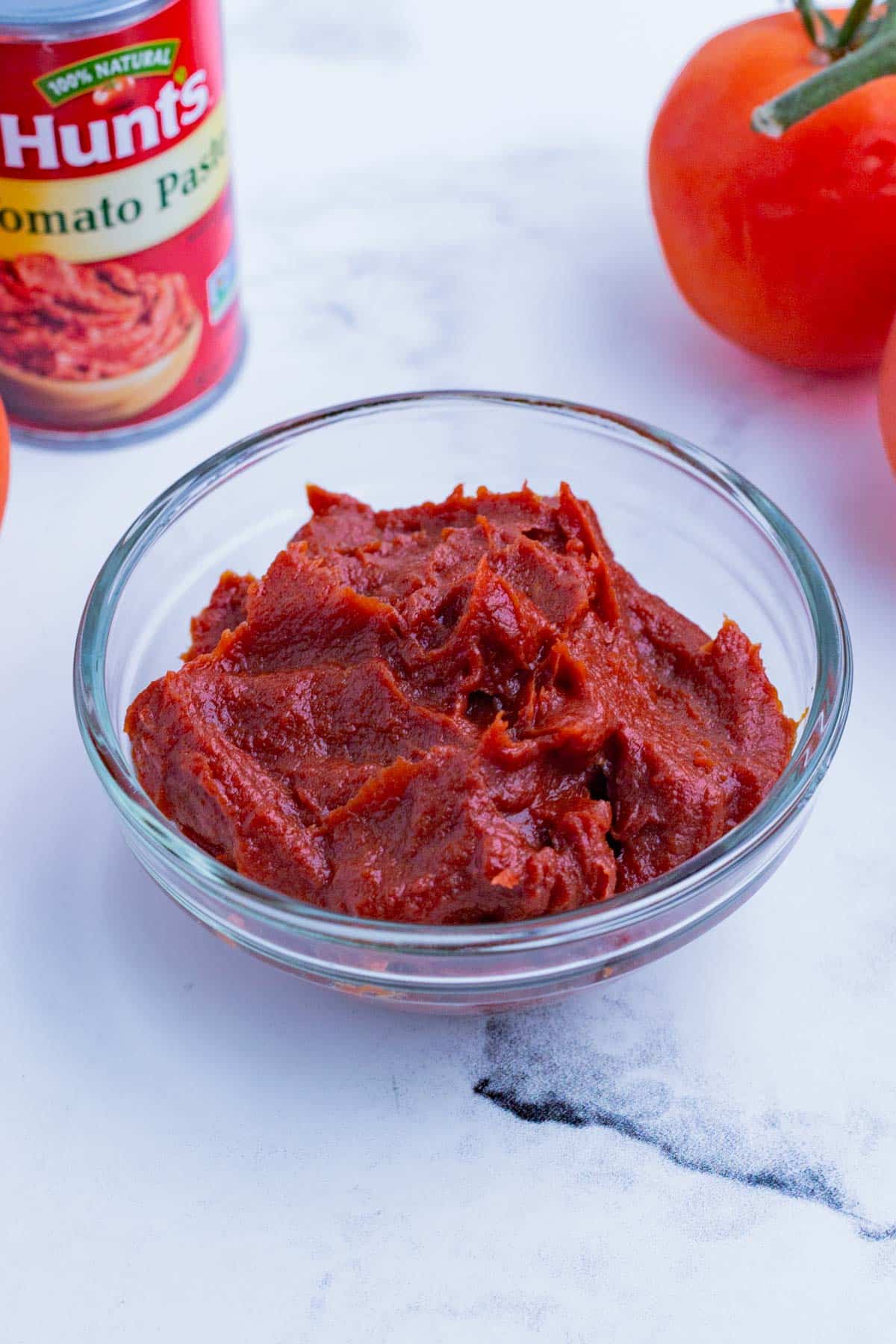 A bowl of tomato paste with a can and fresh tomato on the counter.