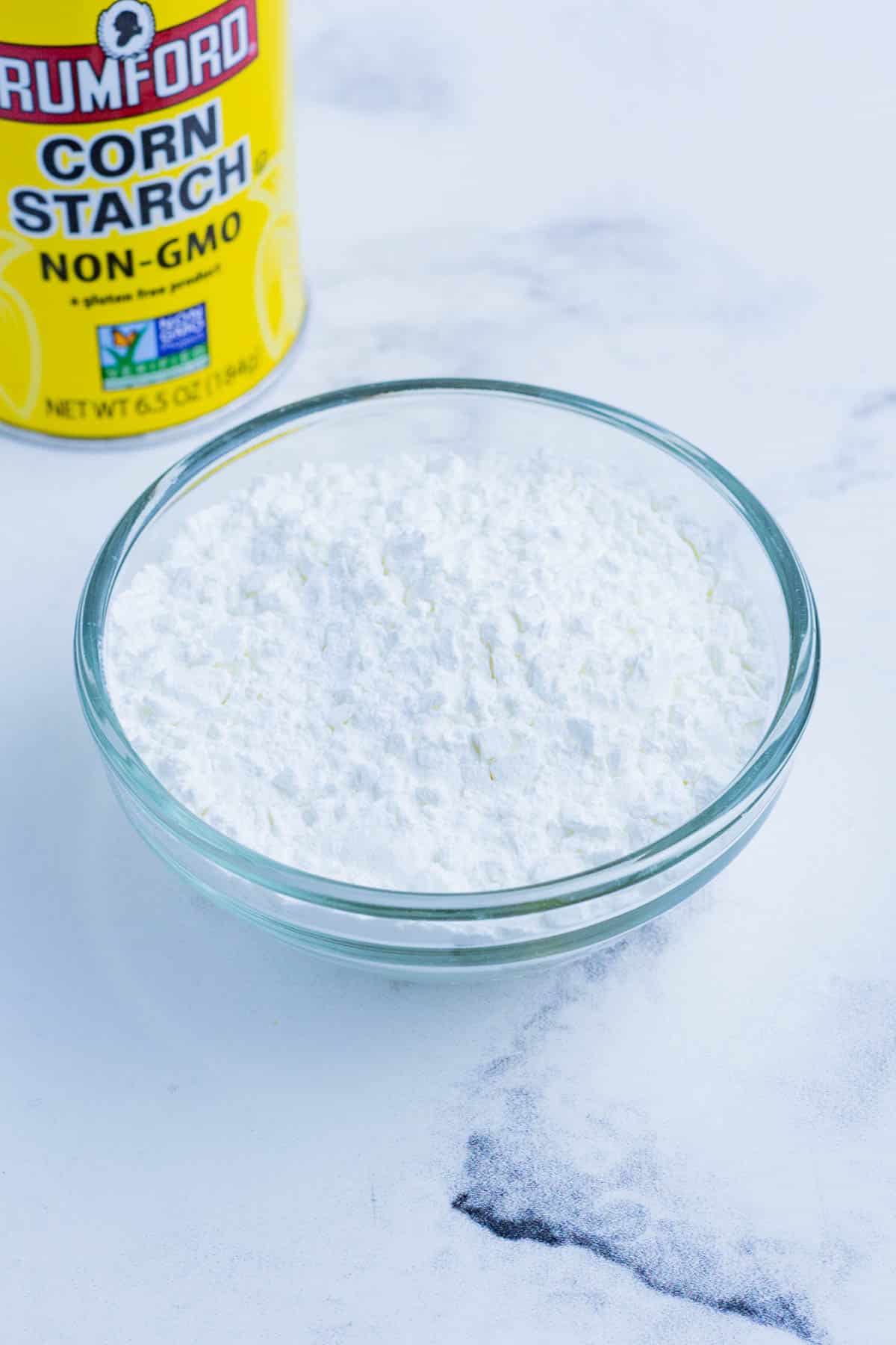 Cornstarch in a small, glass bowl on the countertop with the original cornstarch container in the background.