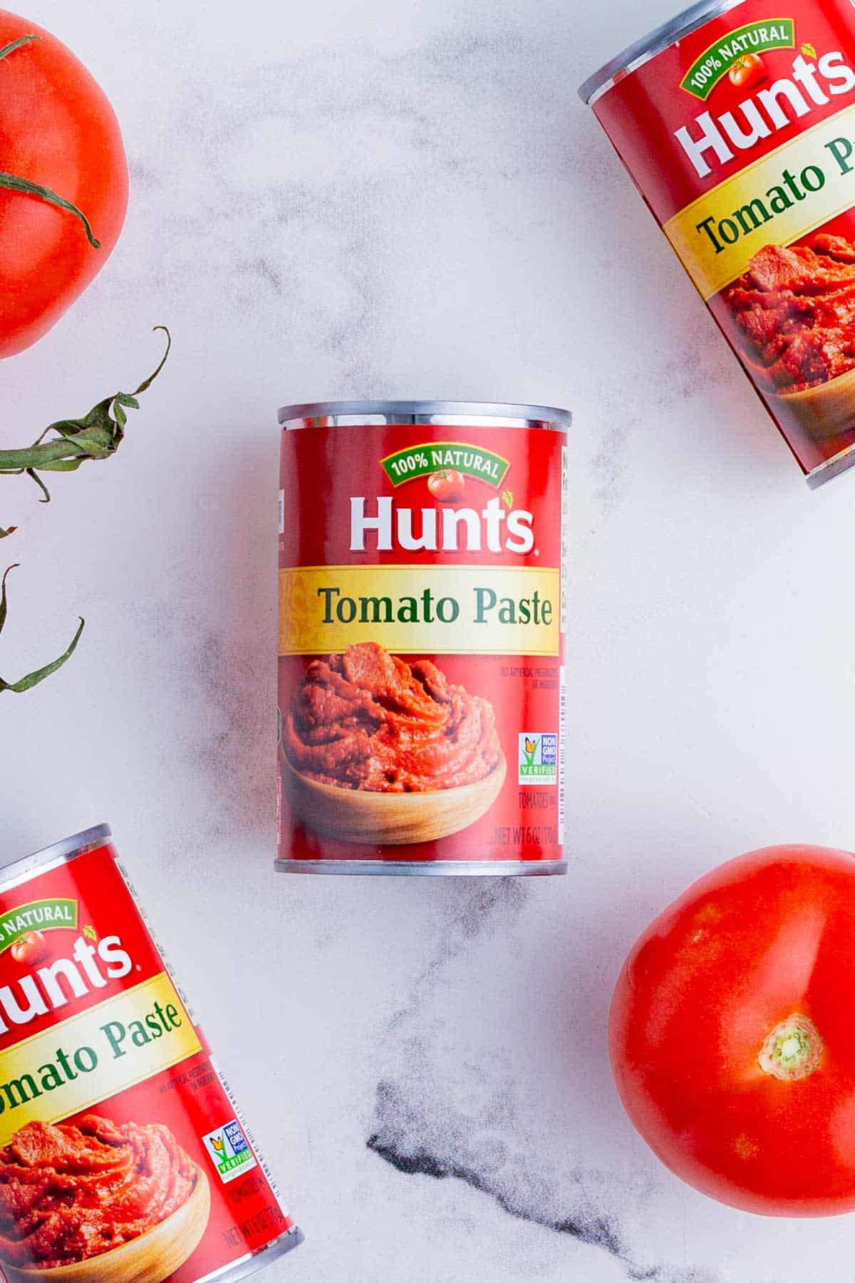 Several cans of tomato paste with fresh, whole tomatoes.