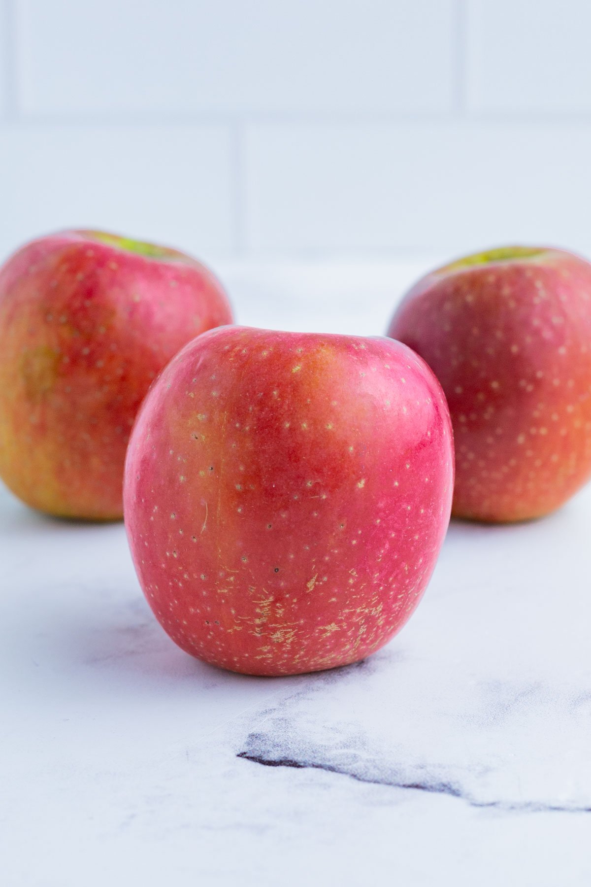 3 Fuji apples on the counter top.