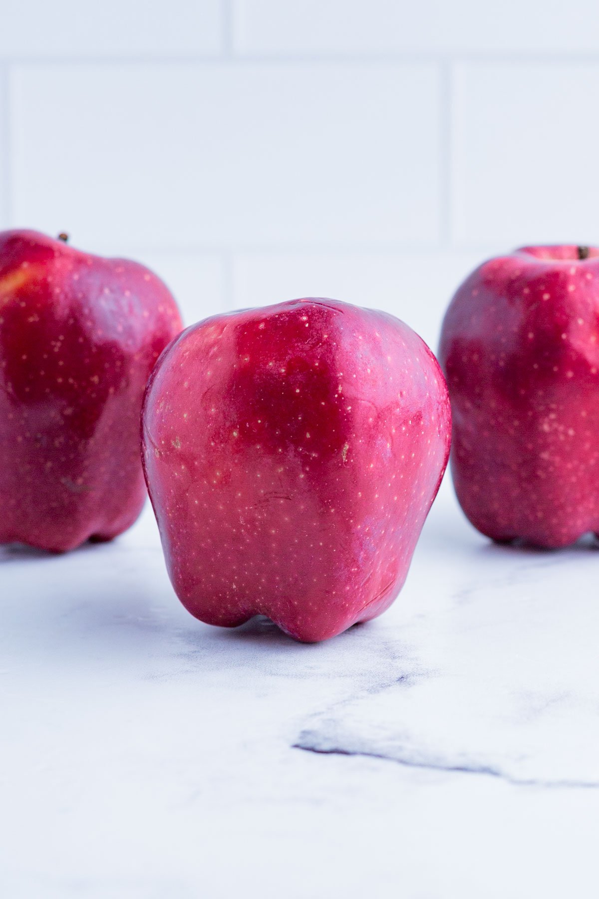 3 Red Delicious apples on the counter top.