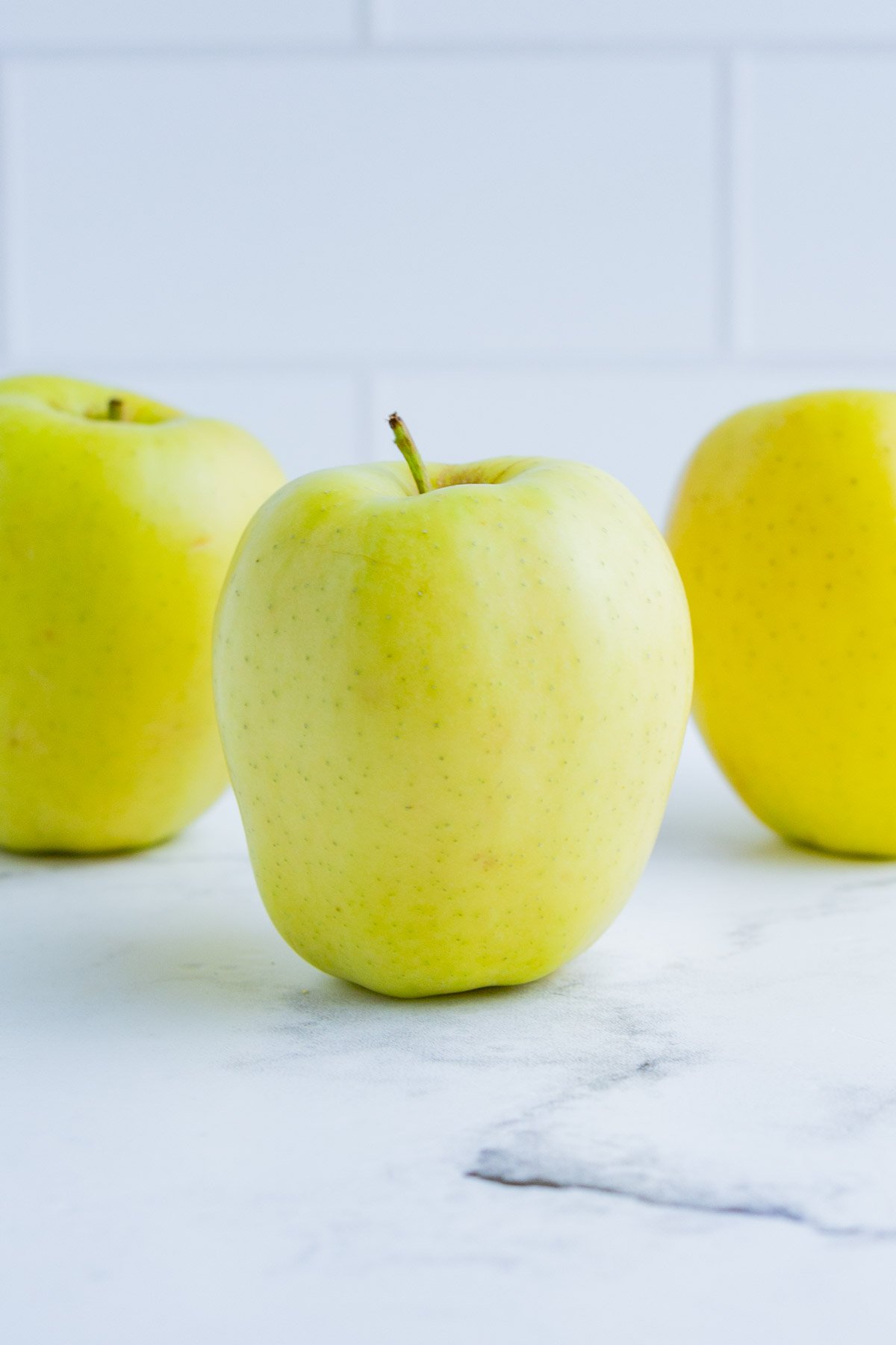 3 Golden Delicious apples on the counter top.