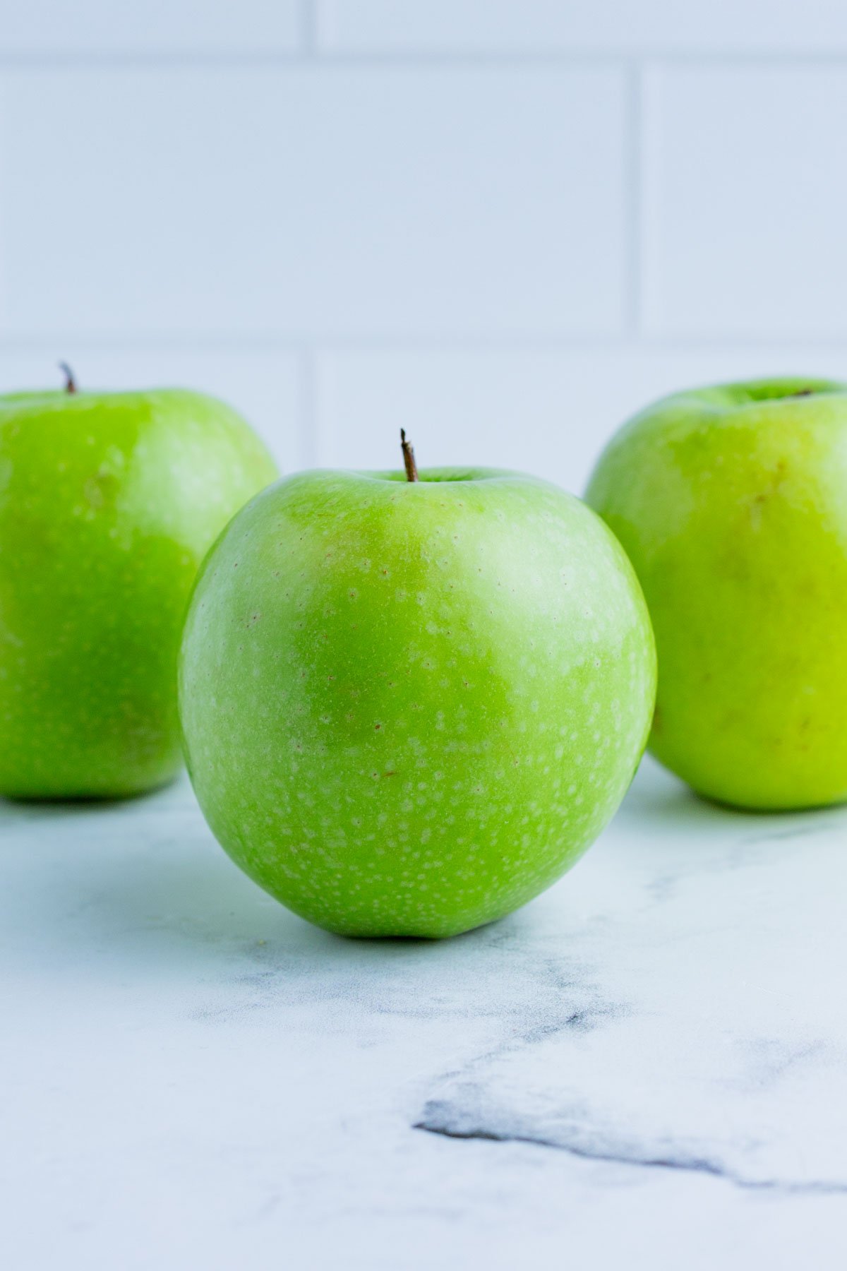 3 Granny Smith apples on the counter top.