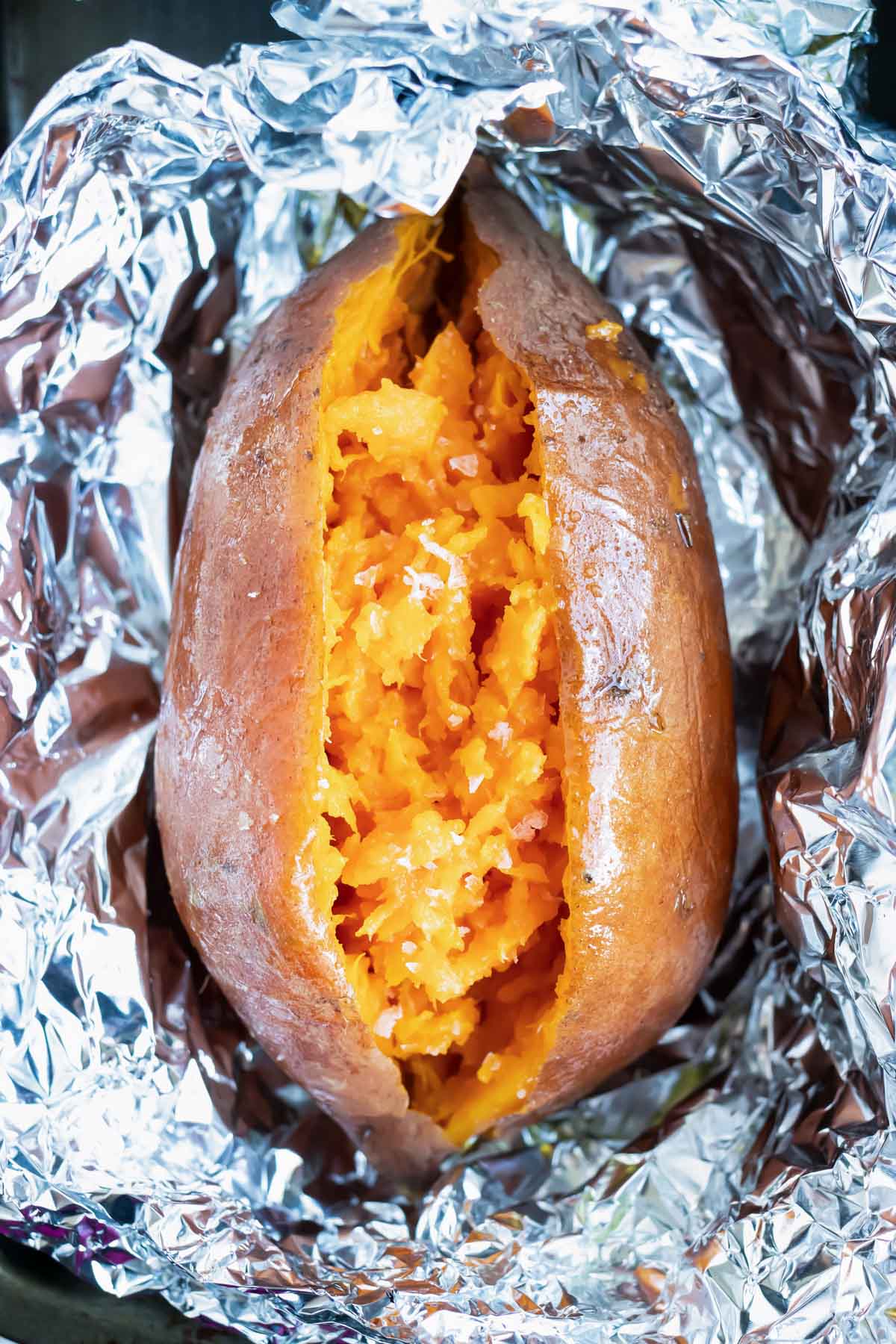 A sweet potato that has been cut in half and has been baked in the oven and wrapped in foil.