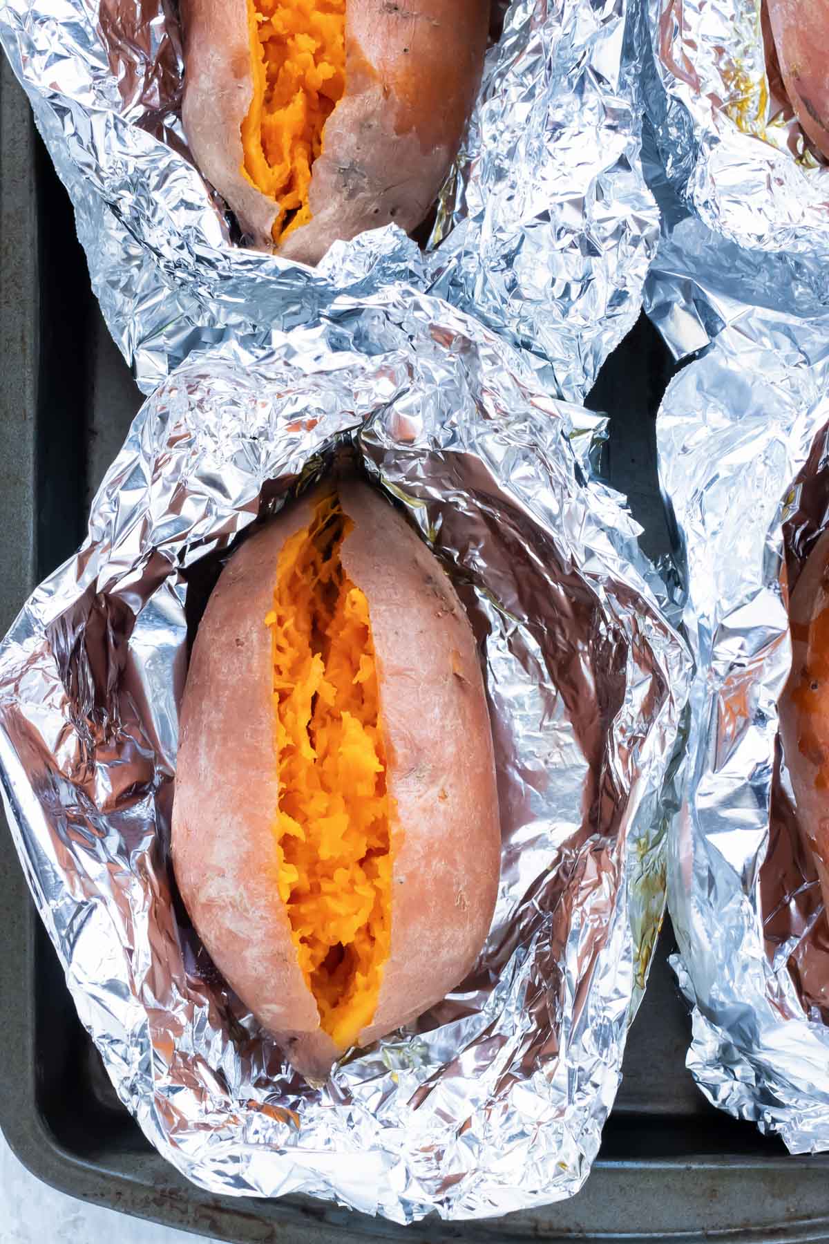 Four sweet potatoes that have been baked on a sheet pan in the oven.