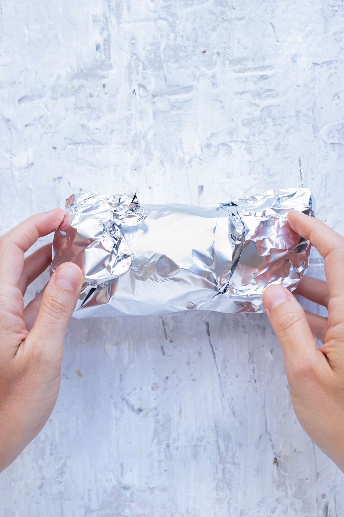 A hand rolls a sweet potato in foil.