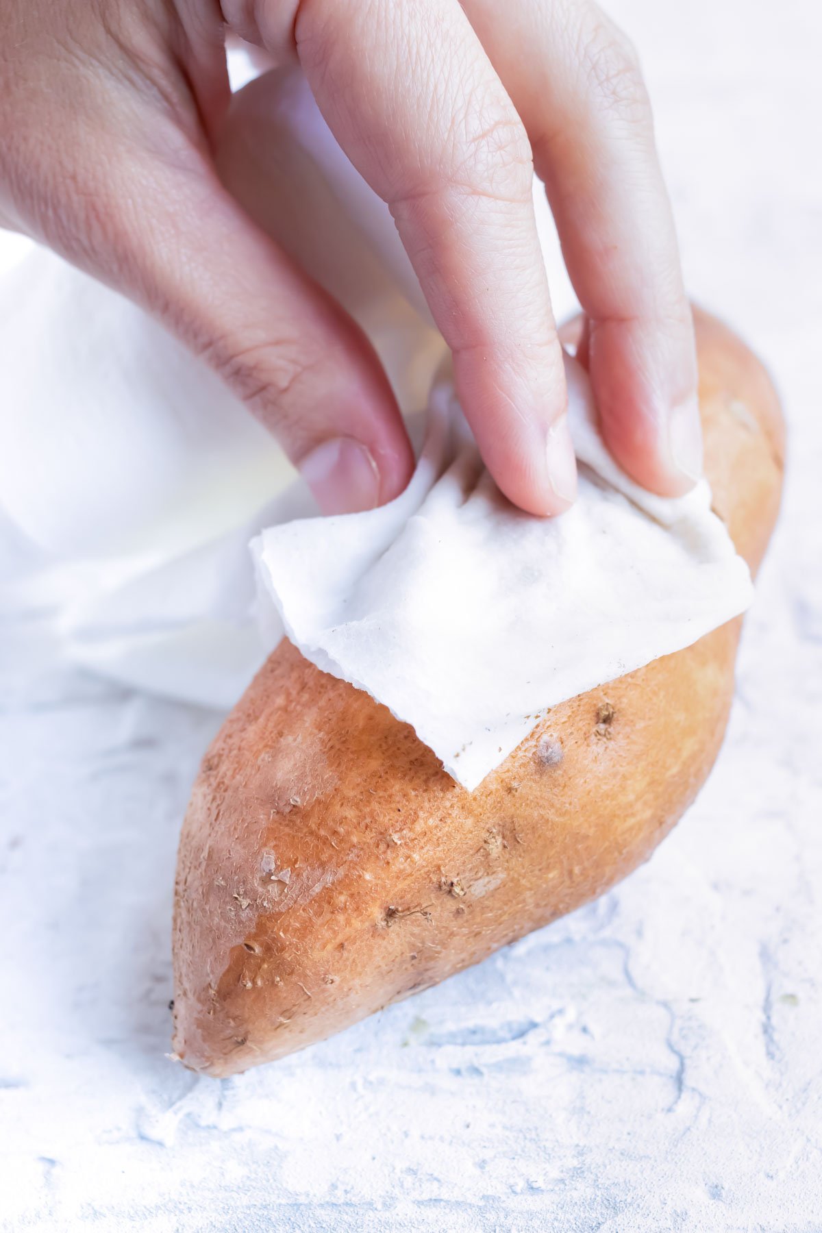A sweet potato being scrubbed clean before roasting.