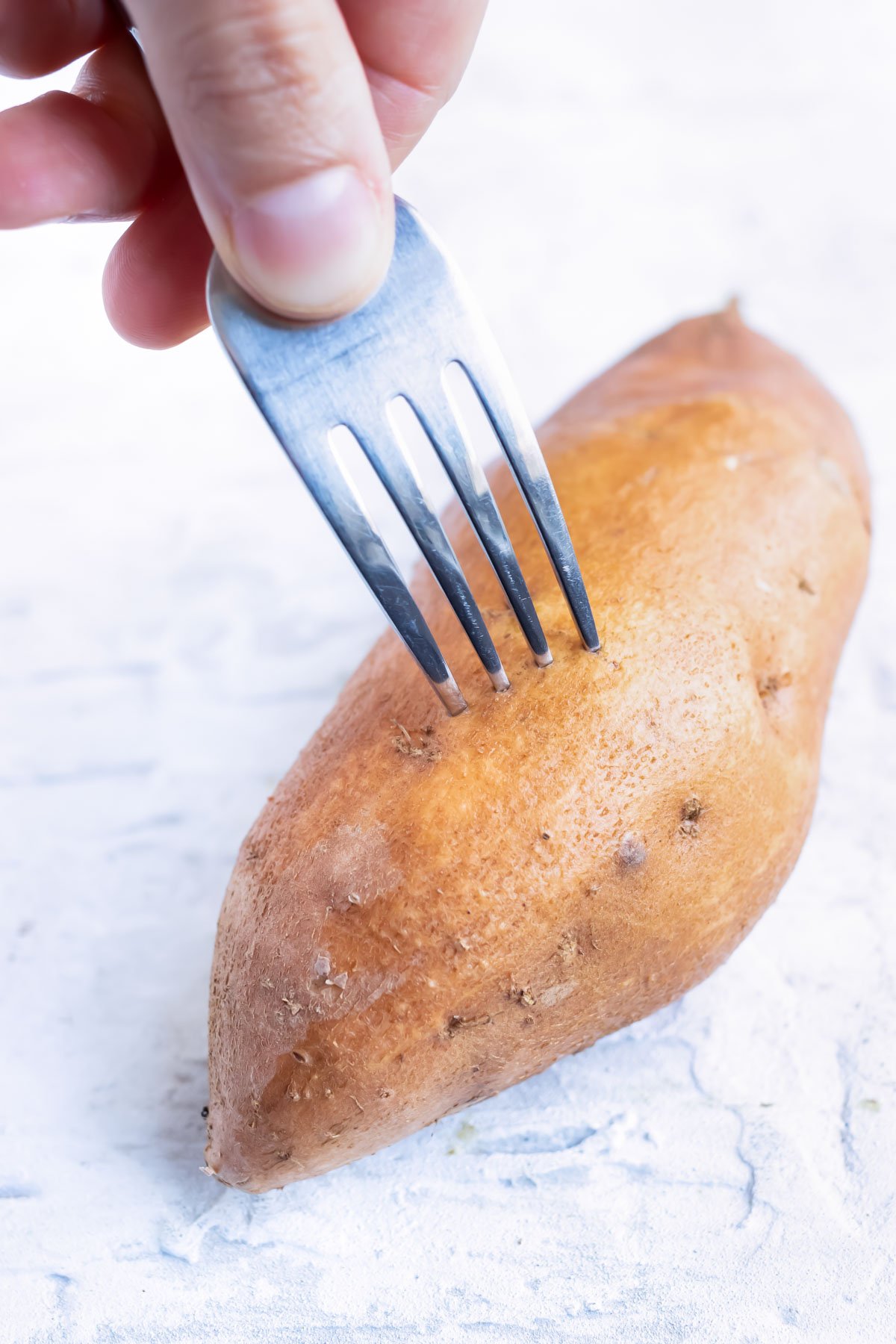 A sweet potato is poked with a fork before baking.