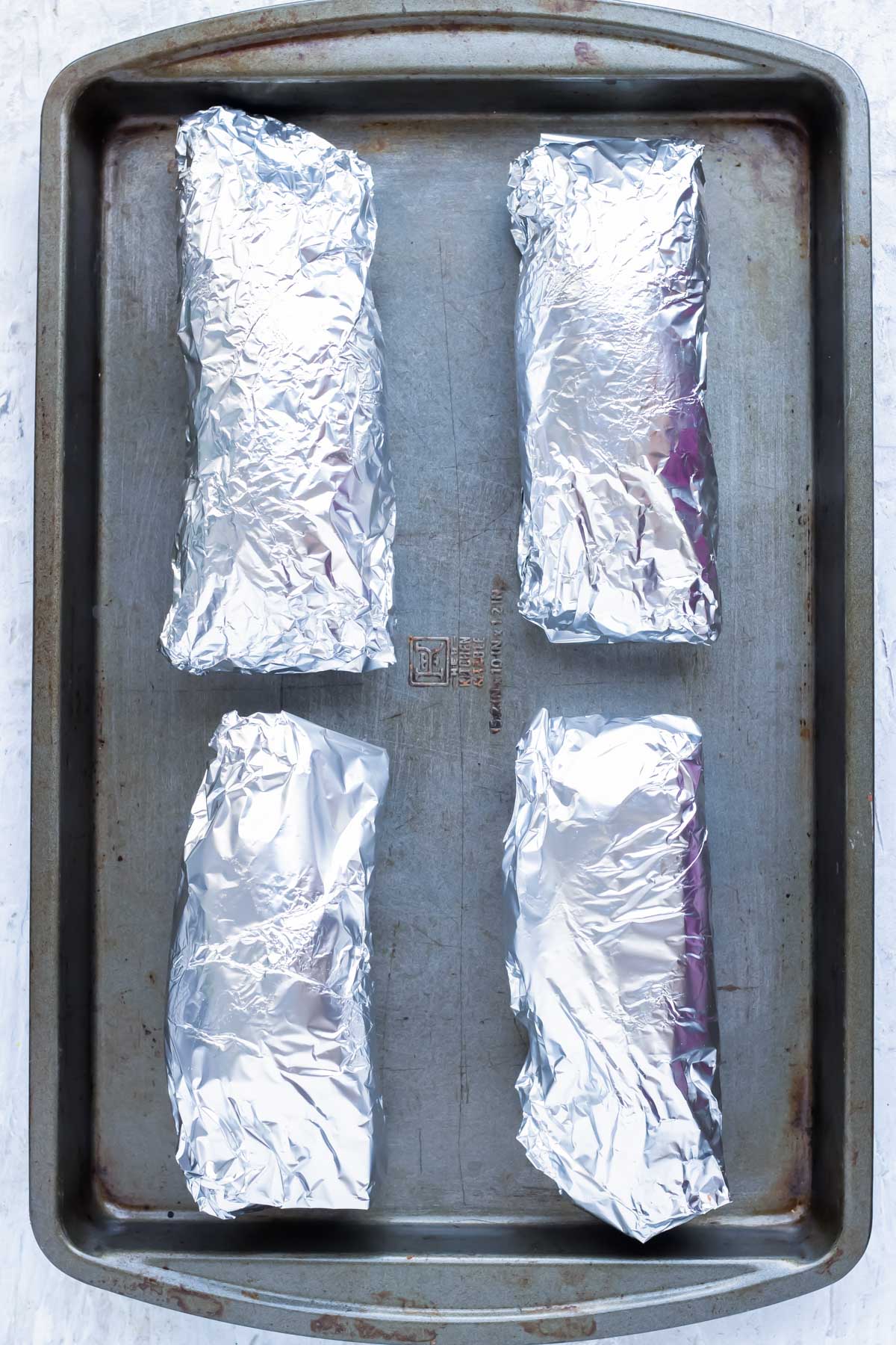 Four sweet potatoes are wrapped in aluminum foil and to be baked in the oven.