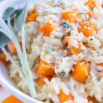 Smooth and creamy butternut squash risotto is served with fresh herbs and topped with parmesan cheese.