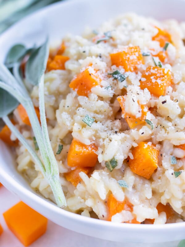 Smooth and creamy butternut squash risotto is served with fresh herbs and topped with parmesan cheese.