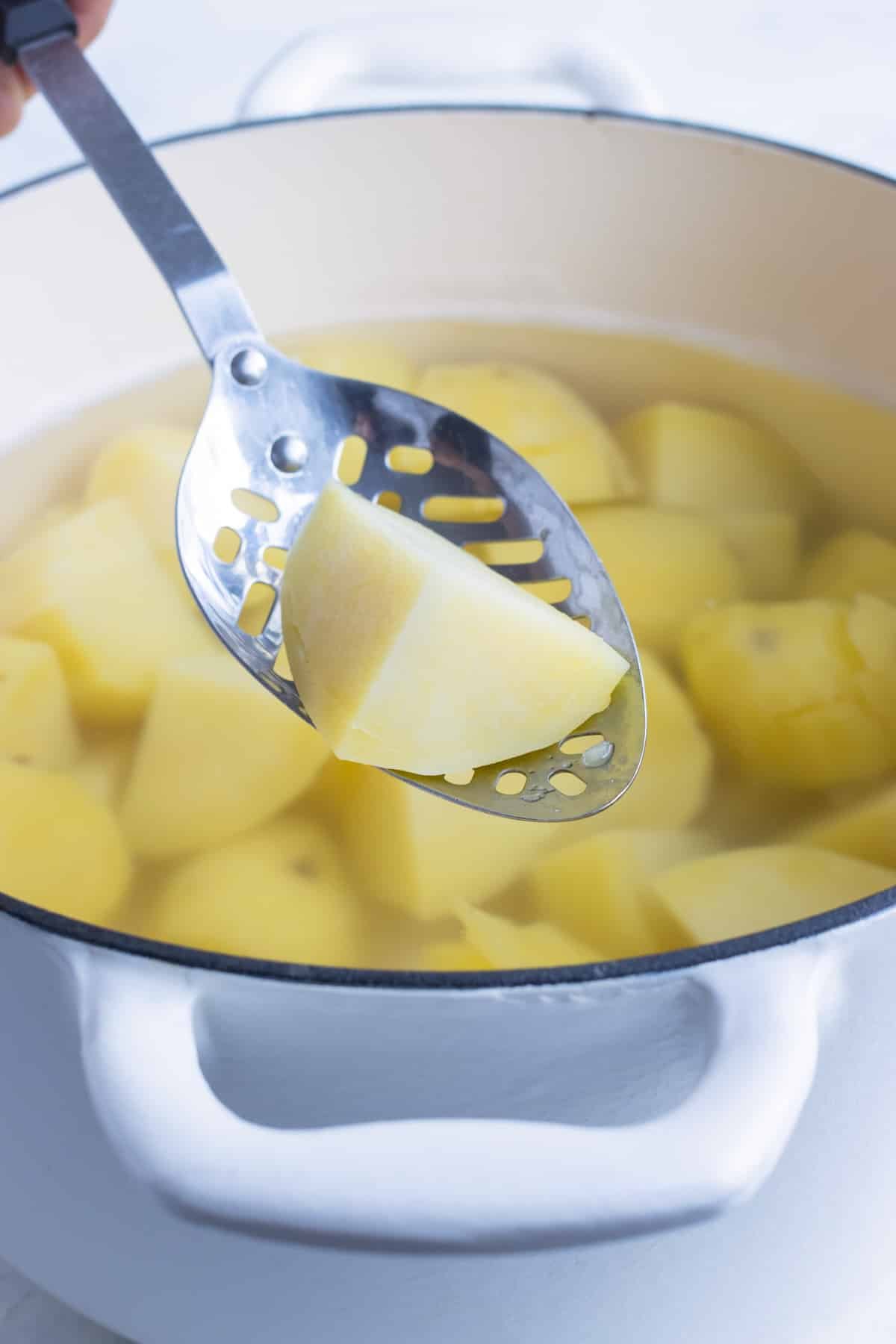 A cubed potato being scooped out of boiling water.