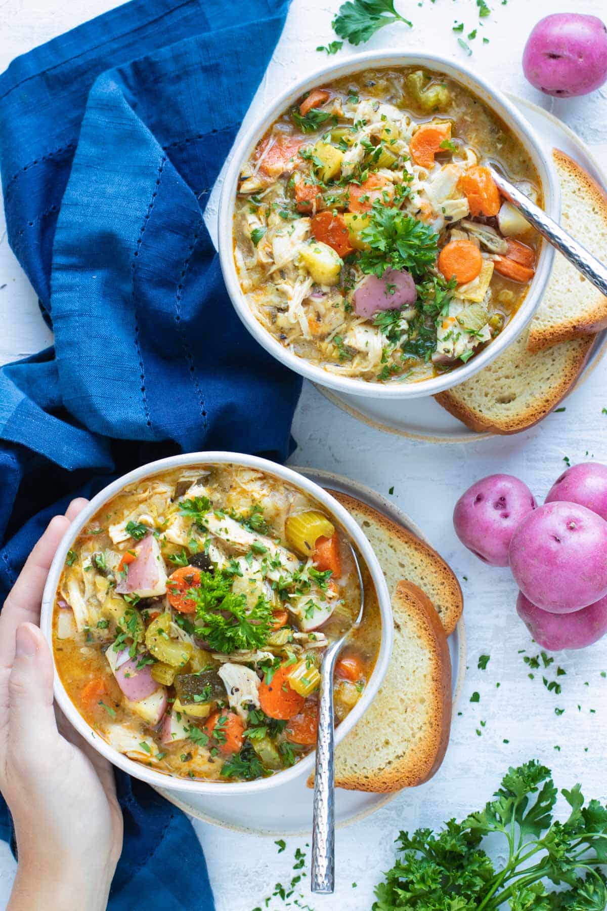 Two white bowls with a blue napkin that are full of a chicken vegetable soup recipe made in the Instant Pot.