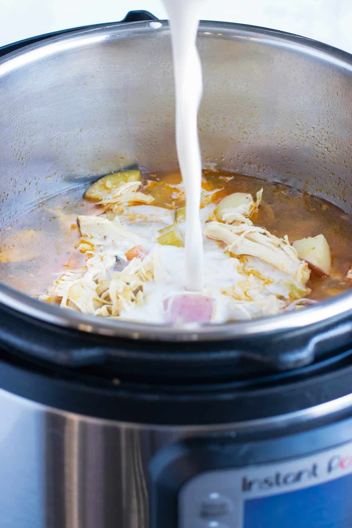 A starch slurry of almond milk and tapioca starch being poured into an Instant Pot to thicken up a chicken vegetable soup recipe.