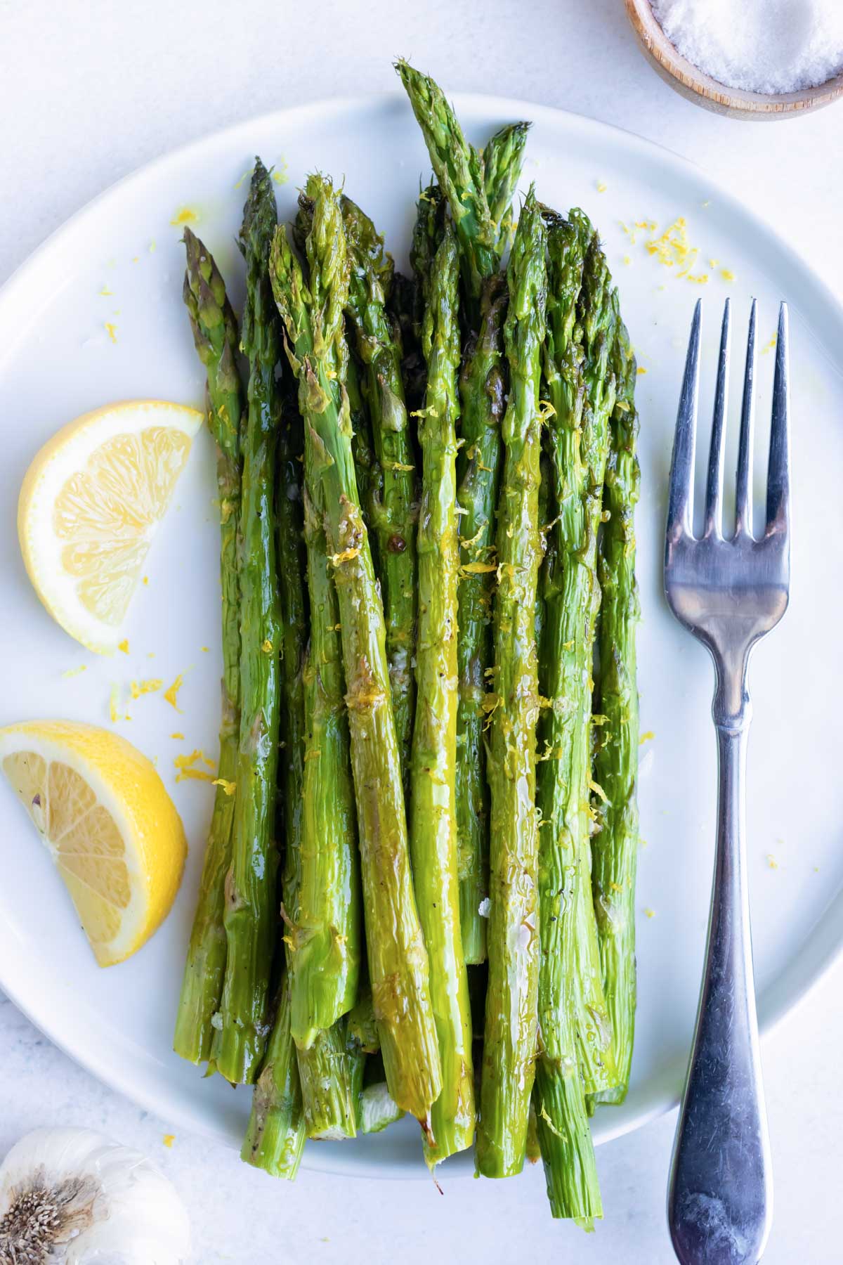 A serving plate full of bright green and tender asparagus spears that were oven-roasted with garlic and lemon juice.
