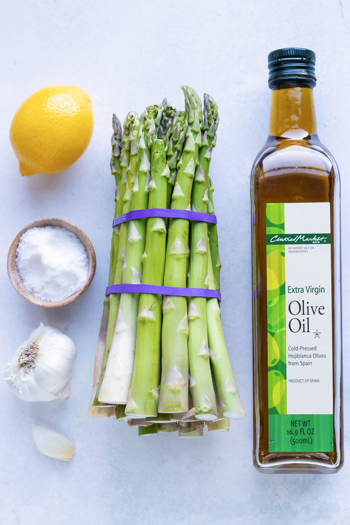 A bunch of asparagus, olive oil, lemon, salt, and garlic as the ingredients for a roasted asparagus recipe.
